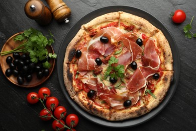 Photo of Tasty pizza with cured ham, olives, tomatoes and parsley on black table, top view