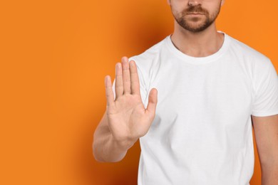 Man showing stop gesture on orange background, closeup with space for text