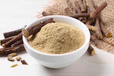 Photo of Powder in bowl and dried sticks of liquorice root on white table, closeup