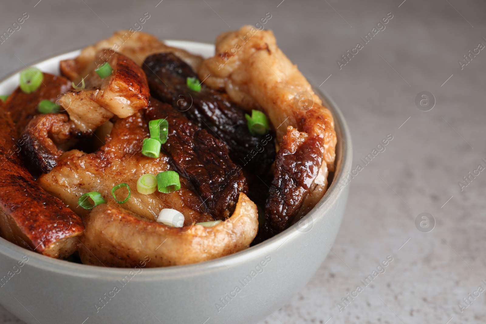 Photo of Bowl with tasty fried pork fatback slices and green onion on grey table, closeup