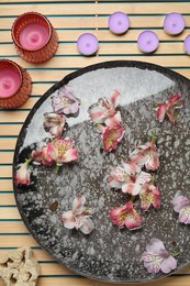 Bowl of water with flowers, candles and loofah on wooden mat, flat lay. Spa treatment