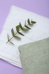 Photo of Different soft towels and eucalyptus branch on violet background, top view