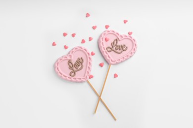 Photo of Chocolate heart shaped lollipops and sprinkles on white background, flat lay