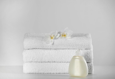 Photo of Soft folded towels, orchid flowers and dispenser on white table