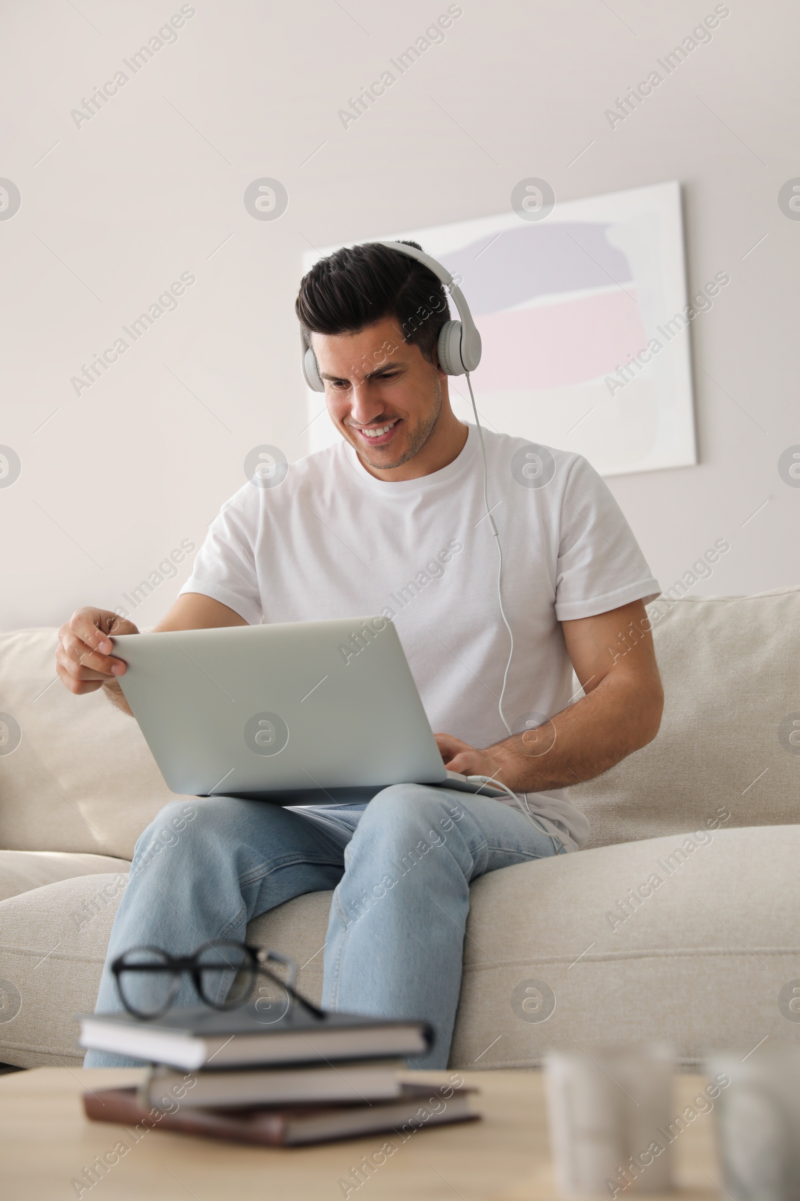 Photo of Man with laptop and headphones sitting on sofa at home