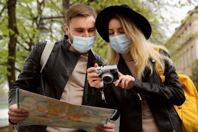 Photo of Couple of tourists in medical masks with map and camera on city street