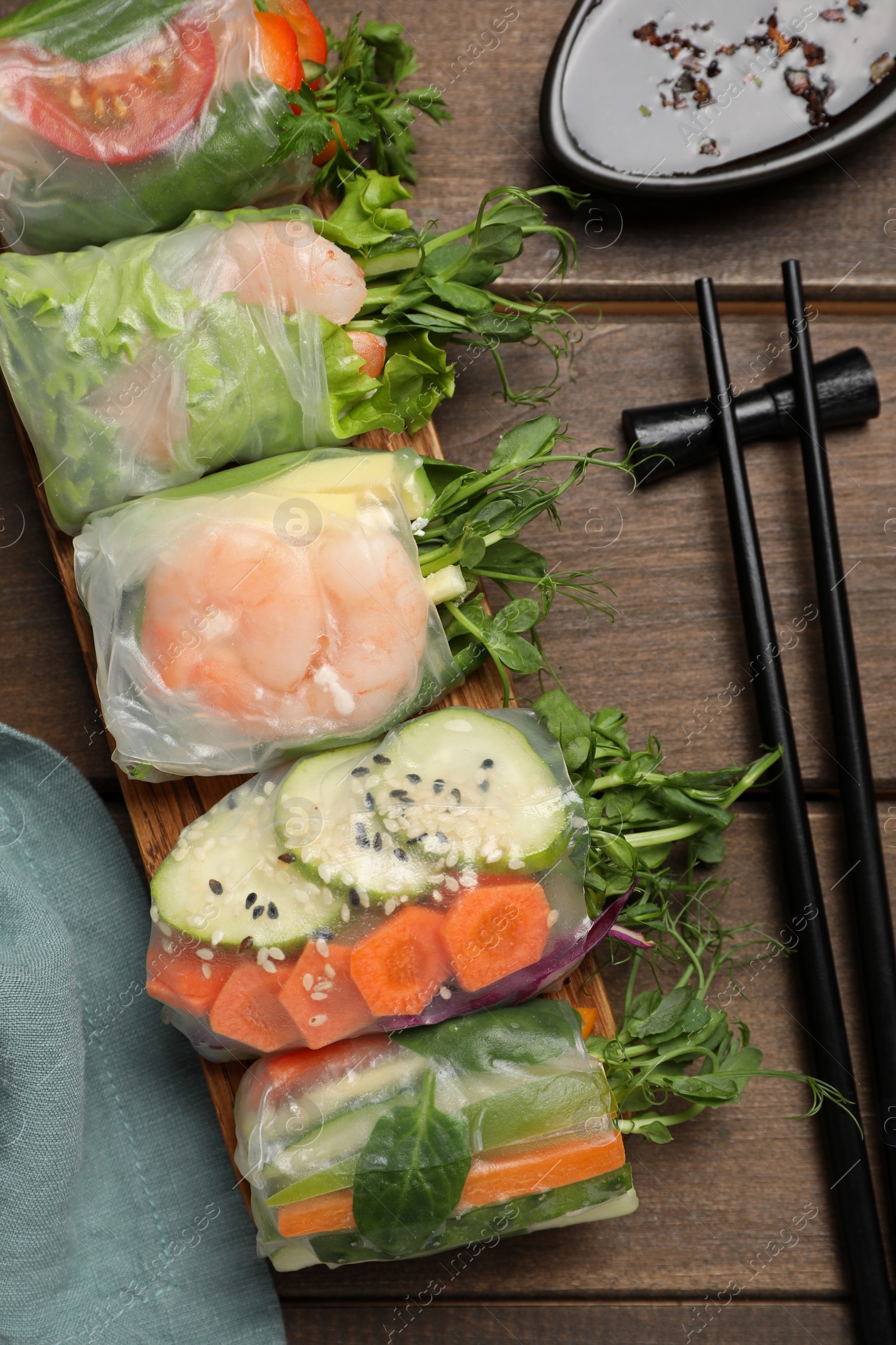 Photo of Many different delicious rolls wrapped in rice paper on wooden table, flat lay