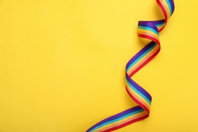 Photo of Rainbow ribbon on yellow background, top view with space for text. LGBT pride