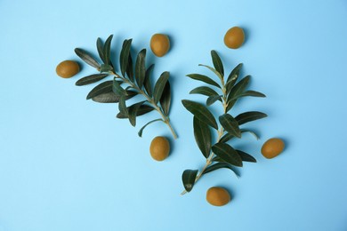 Fresh olives and green leaves on light blue background, flat lay