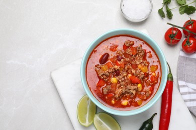 Photo of Bowl with tasty chili con carne and ingredients on white table, flat lay. Space for text