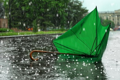 Image of Broken green umbrella in park on rainy day with hail