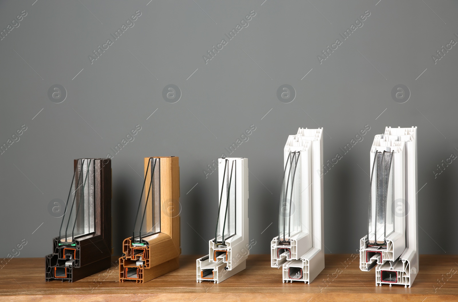 Photo of Samples of modern window profiles on table against gray wall. Installation service