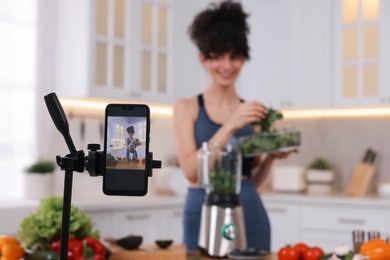 Photo of Food blogger cooking while recording video in kitchen, focus on smartphone