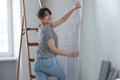 Woman hanging stylish gray wallpaper in room