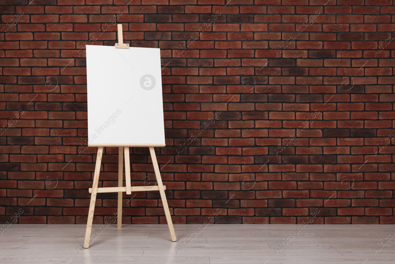 Photo of Wooden easel with blank canvas near brick wall indoors. Space for text