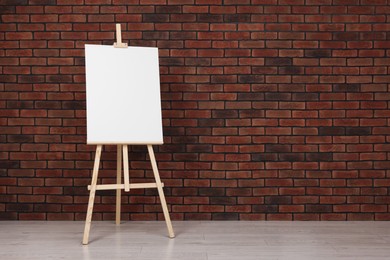 Photo of Wooden easel with blank canvas near brick wall indoors. Space for text