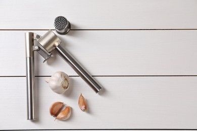 Metal press and garlic on white wooden table, flat lay. Space for text