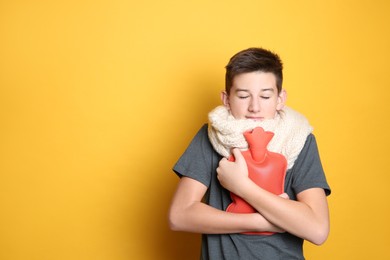 Photo of Sick teenage boy with hot water bottle on yellow background. Space for text