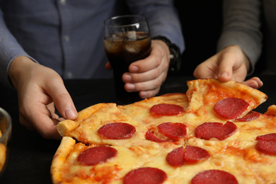 Photo of Friends taking tasty pepperoni pizza at table, closeup