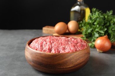 Photo of Raw ground meat in bowl and different products on grey table