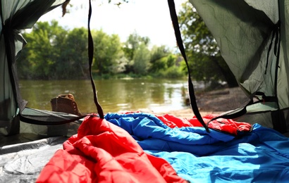 Camping tent with sleeping bag near lake, view from inside