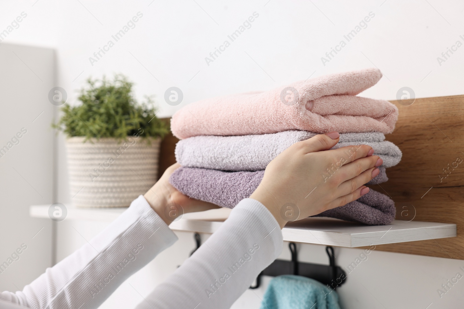 Photo of Woman stacking clean towels on shelf indoors, closeup