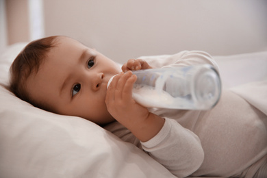 Photo of Cute little baby with bottle lying in comfortable crib. Bedtime