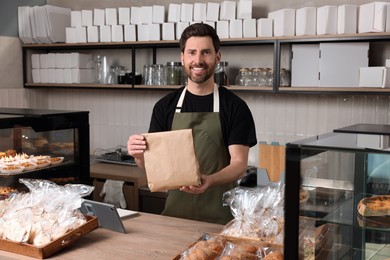 Photo of Happy seller with paper bag at cashier desk in bakery shop