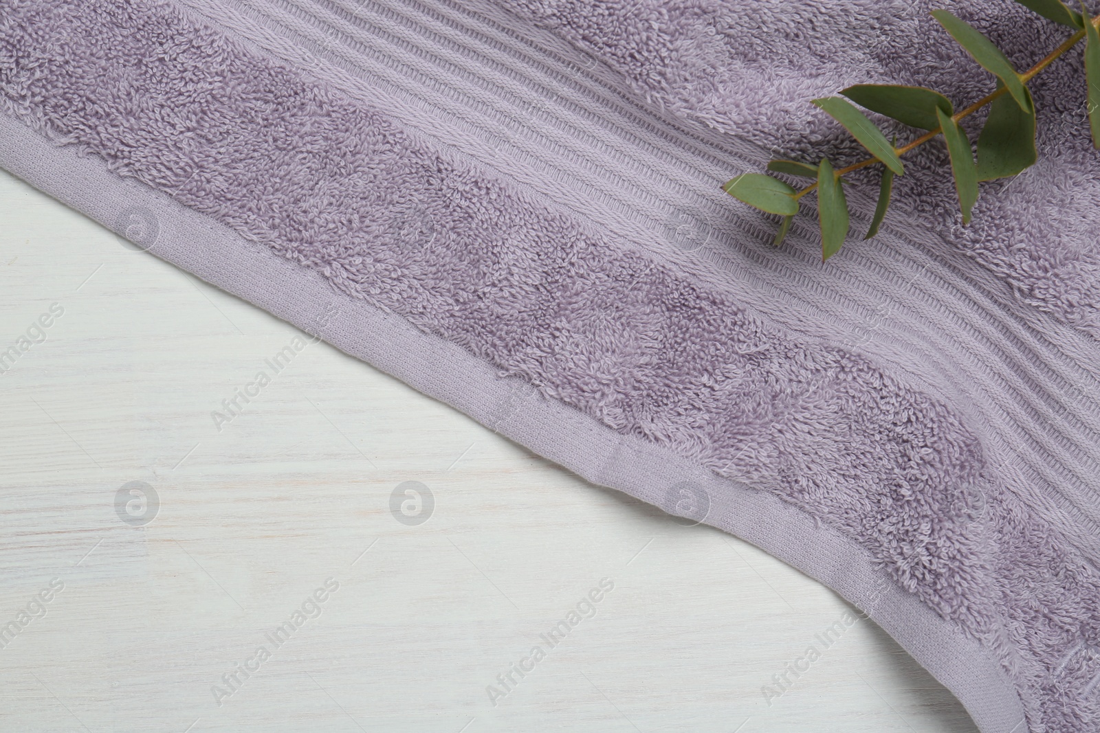 Photo of Violet terry towel and eucalyptus branch on light wooden table, top view. Space for text