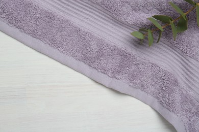 Photo of Violet terry towel and eucalyptus branch on light wooden table, top view. Space for text