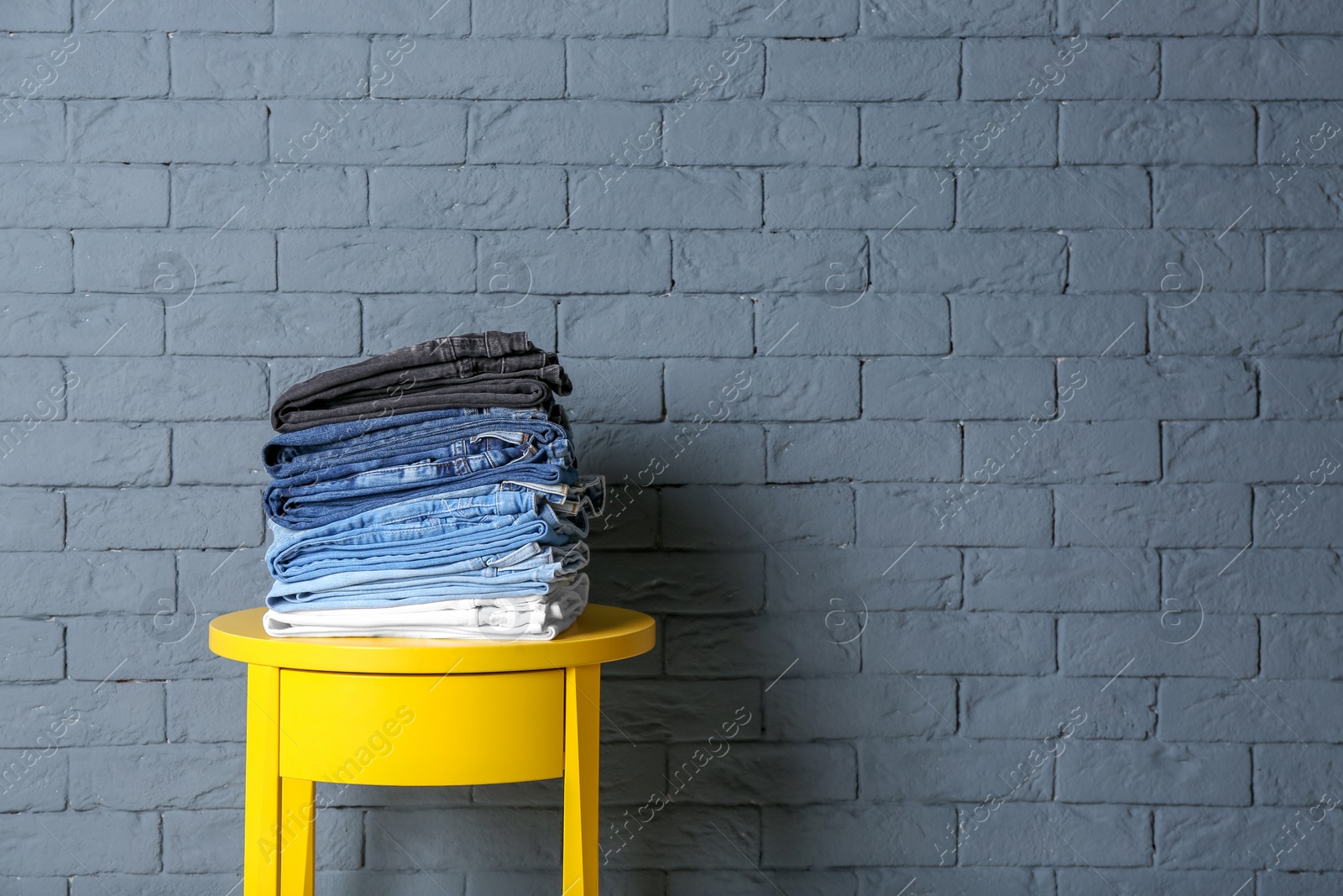 Photo of Stack of different jeans on table against brick wall