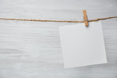 Photo of Clothespin with blank notepaper on twine against white wooden background. Space for text