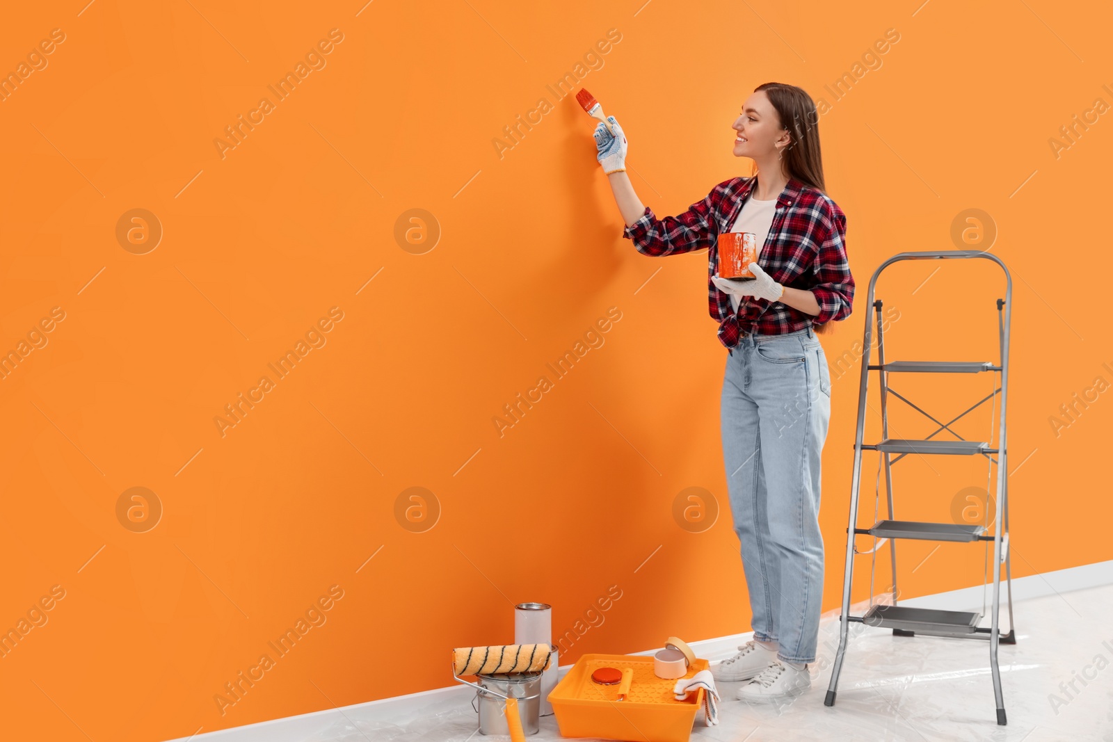 Photo of Designer painting orange wall with brush indoors, space for text