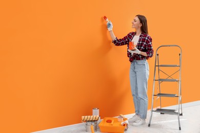 Designer painting orange wall with brush indoors, space for text
