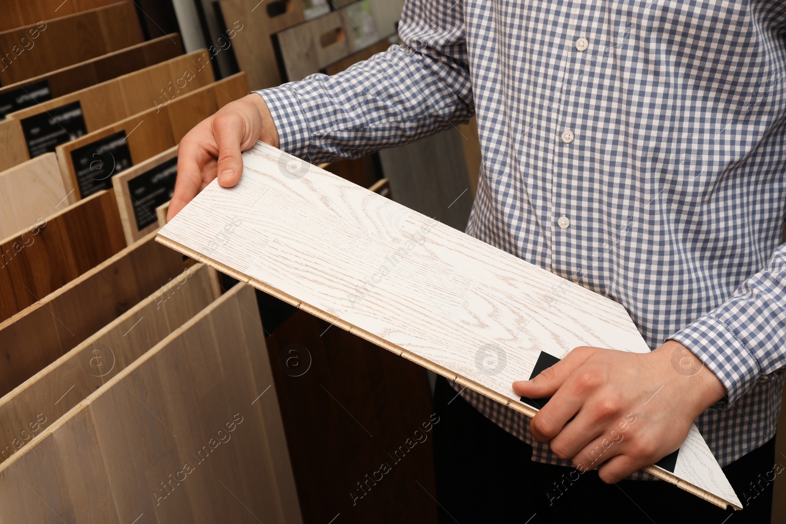 Photo of Man with sample of light wooden flooring in shop, closeup