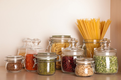 Glass jars with different types of groats on wooden shelf