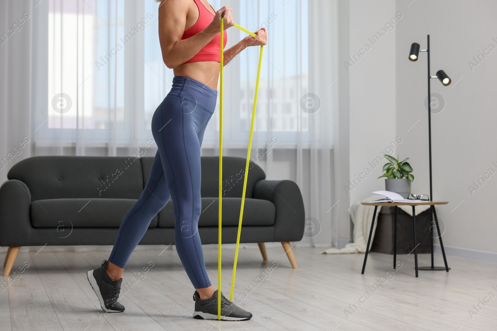 Photo of Woman doing exercise with fitness elastic band at home, closeup