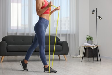 Photo of Woman doing exercise with fitness elastic band at home, closeup