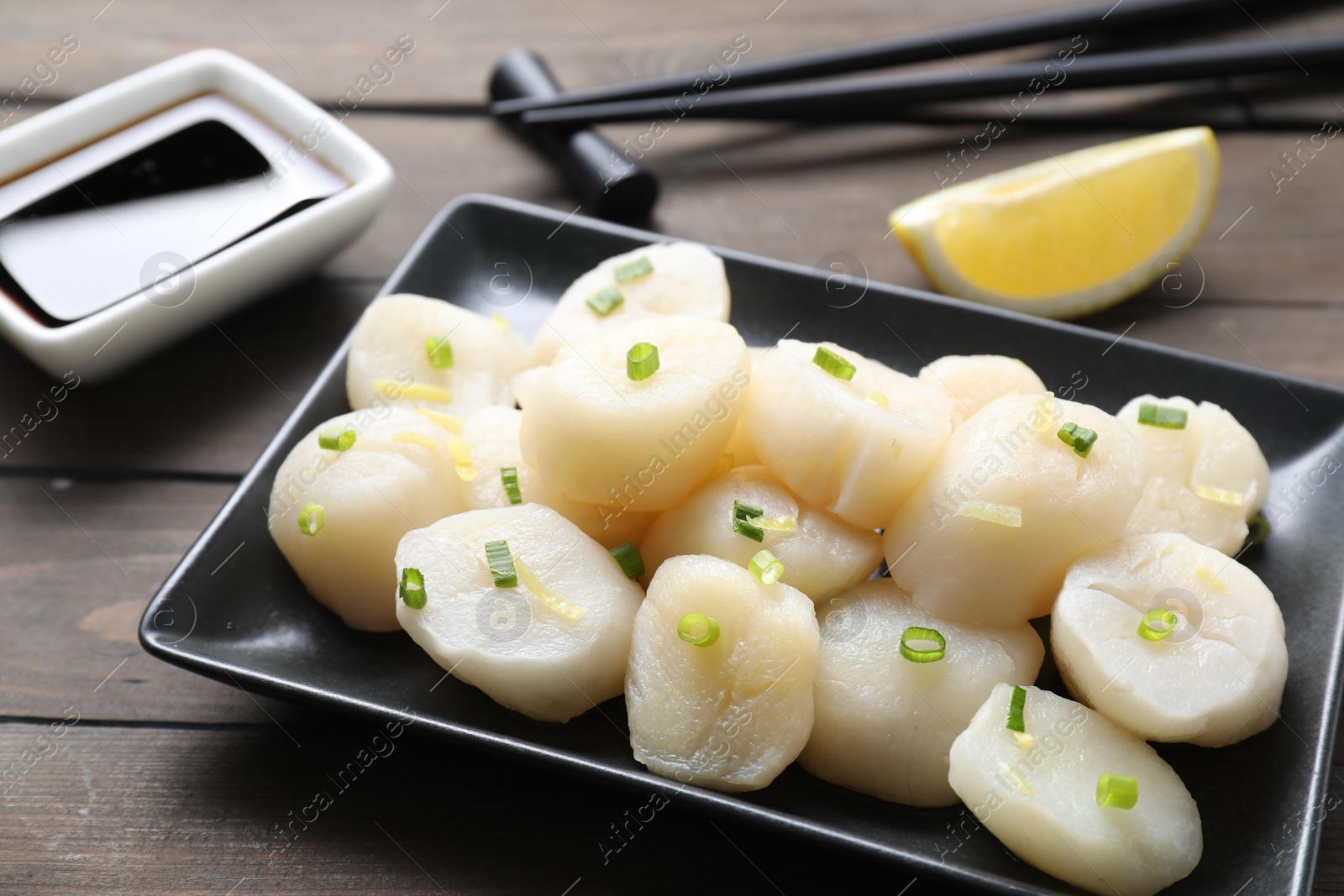 Photo of Raw scallops with green onion on wooden table, closeup