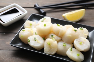 Photo of Raw scallops with green onion on wooden table, closeup