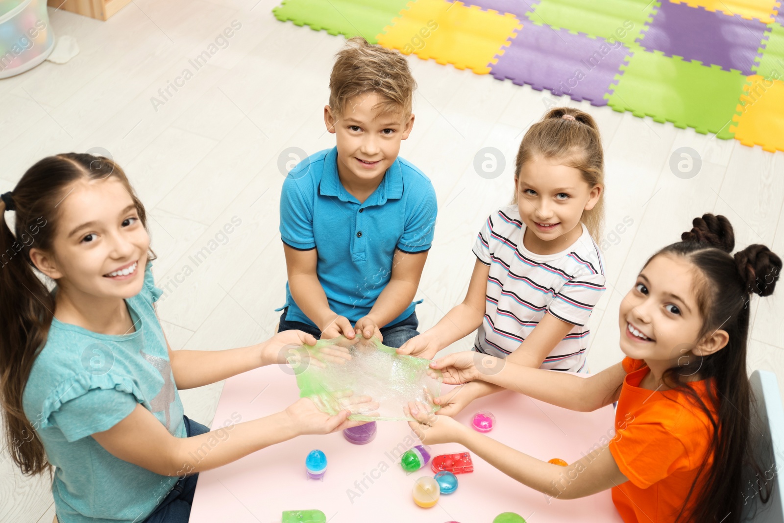 Photo of Happy children playing with slime at table indoors, above view