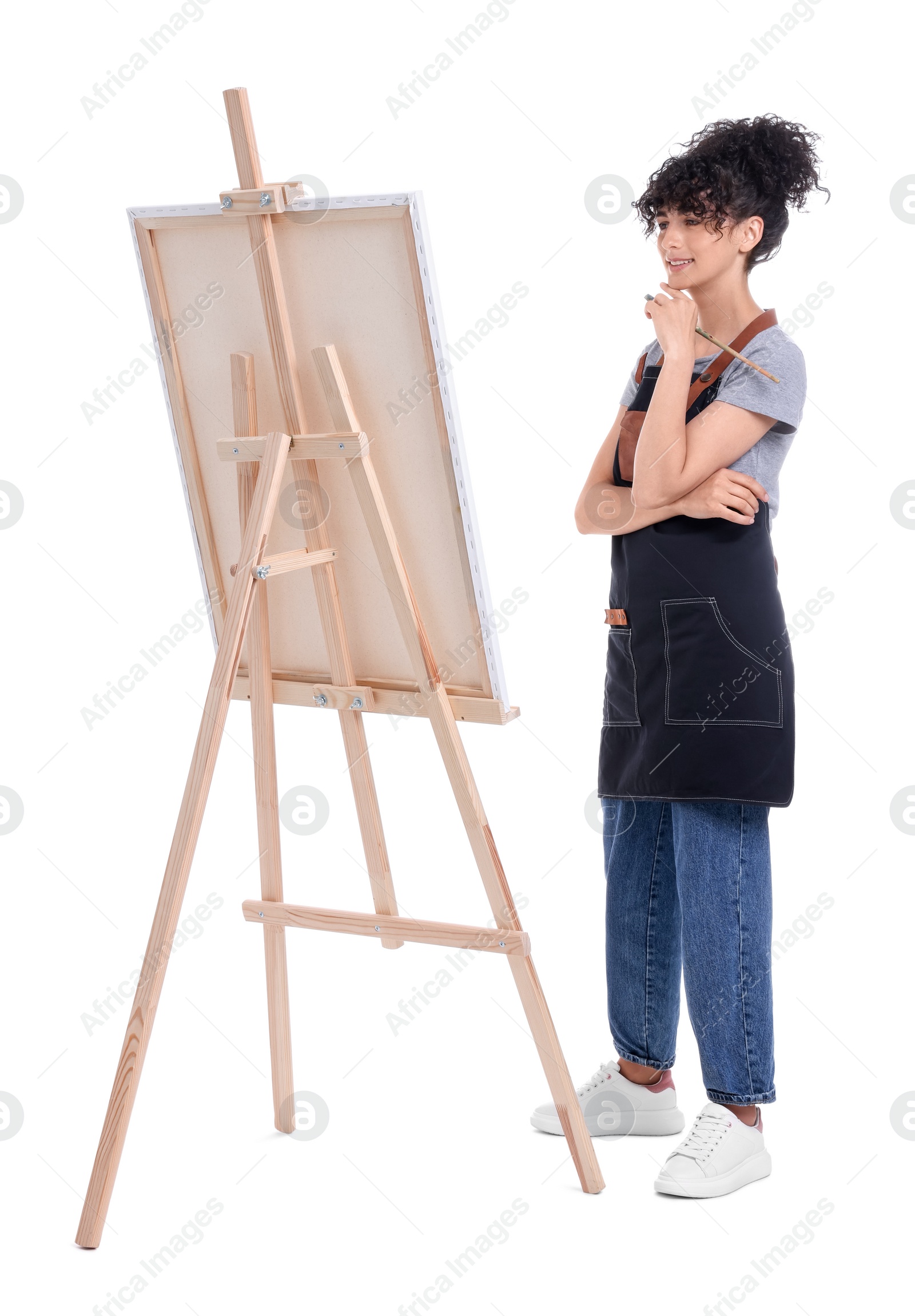 Photo of Young woman holding brush near easel with canvas against white background