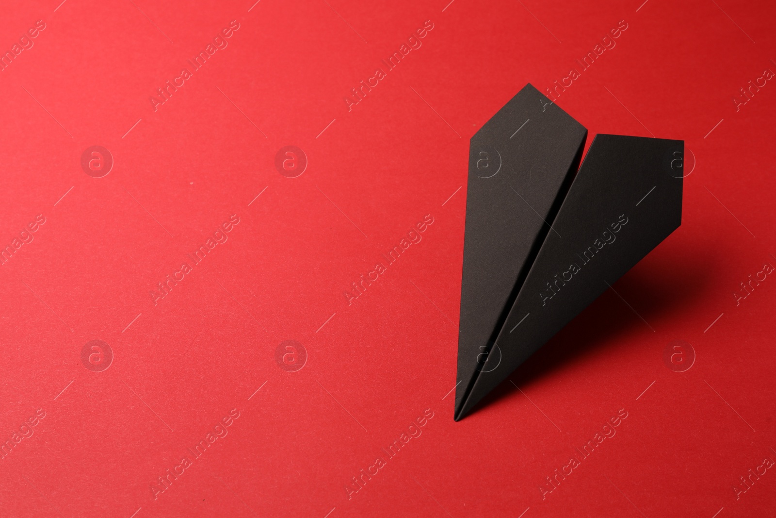 Photo of Handmade black paper plane on red background, space for text