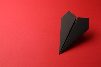 Handmade black paper plane on red background, space for text