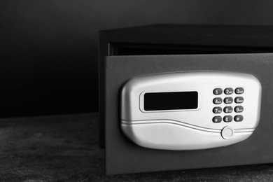 Photo of Black steel safe with electronic lock on grey table against dark background, closeup