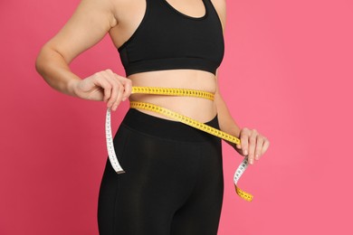 Photo of Woman measuring waist with tape on pink background, closeup