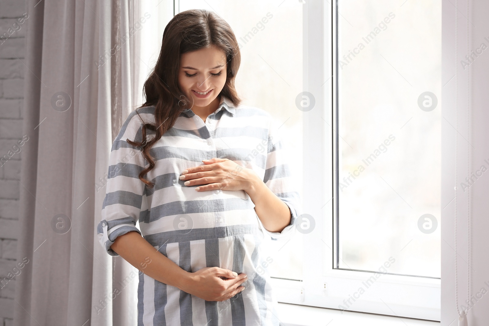 Photo of Beautiful pregnant woman near window at home