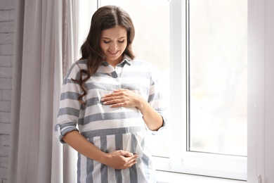 Photo of Beautiful pregnant woman near window at home