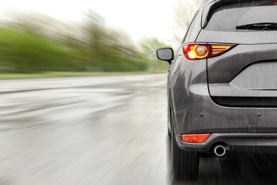 Image of Black car driving at high speed on rainy day outdoors, closeup with motion blur effect. Space for text