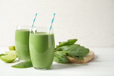 Photo of Glasses of healthy green smoothie with fresh spinach on white wooden table against light background. Space for text